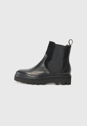 Bottine noire en cuir avec des accents en velours et des panneaux latéraux en élastique. Elle dispose d'une semelle en caoutchouc épaisse et d'une languette à l'arrière.
