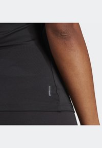 Schwarzes Sportshirt aus atmungsaktivem Material mit glatter Textur und einem Logoetikett mit der Aufschrift "AEROREADY" an der Seitennaht, ohne zusätzliche Verzierungen.