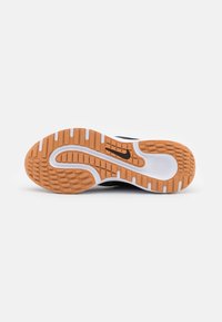 Suela de zapato con una superficie de goma texturizada, que presenta un patrón en naranja y blanco, un diseño curvado y un acento de logo negro.