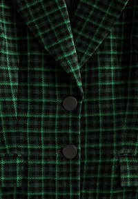 Blazer à carreaux vert foncé et noir avec de larges revers et deux grands boutons noirs à l'avant.