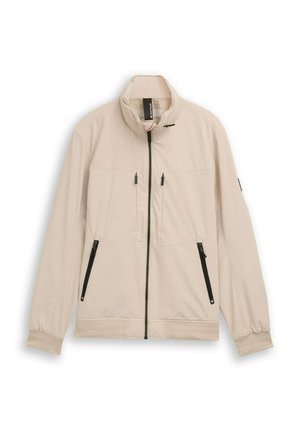 Beige lichtgewicht jack met hoge kraag, ritssluiting aan de voorkant en twee voorzakken met zwarte ritsen. Mouwen met manchetten en een zoombanddetail.
