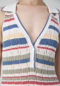 Top de punto multicolor con acanalado vertical, que presenta un escote en V profundo, cuello blanco y botones, en rayas de azul, rojo, verde y amarillo.