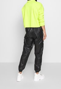 Neongrön kort sweatshirt matchad med glänsande svarta cargobyxor med elastiska ärmslut. Vita chunky sneakers fulländar looken.