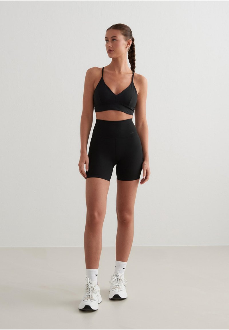 Top deportivo negro de corte cropped con tirantes finos y pantalones cortos negros de cintura alta. Textura suave, diseño ajustado, combinado con zapatillas deportivas blancas y calcetines.