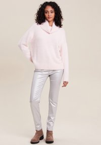 Un pull moelleux rose clair avec un col cheminée, associé à un pantalon brillant argenté slim et des bottines marron. Matériaux texturés et coupe décontractée.