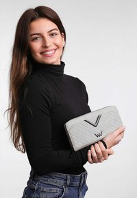 Šedá prošívaná peněženka s elegantním designem, která disponuje černým akcentem a zipovým uzávěrem, držena v ruce na neutrálním pozadí.