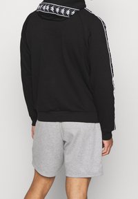 Felpa nera con cappuccio e strisce laterali bianche, in cotone, con motivo grafico sul cappuccio, abbinata a pantaloncini grigi.