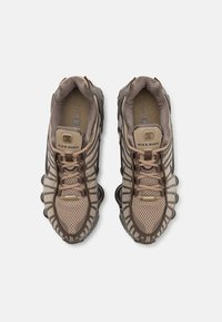 Nike Shox tenisice s gornjim dijelom od prozračnog mrežastog materijala u svijetlosmeđoj boji, tamnosmeđim akcentima, zaobljenim vrhom i prepoznatljivim dizajnom podloge s jastučićima.