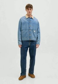 Jeansjacke in Hellblau mit beigem Kragen, Fronttaschen und braunen Knöpfen. Kombiniert mit dunkelblauen Jeans und braunen Schuhen.