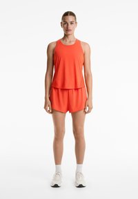 Ensemble de sport orange vif comprenant un haut sans manches et un short assorti. Fabriqué en tissu léger avec une texture douce, idéal pour l'activité.