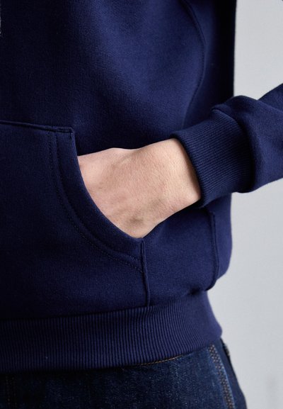 Navyblaues Sweatshirt mit einer Fronttasche, gerippten Bündchen und Saum, das eine glatte Stofftextur und ein figurnahes Design präsentiert.