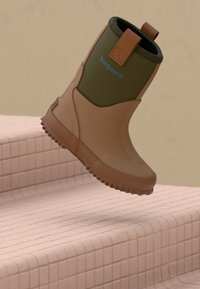 Botte étanche marron et verte avec une languette, flottant au-dessus de marches carrelées roses sur un fond beige.