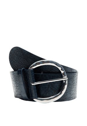 Ceinture en cuir noir texturé avec une grande boucle ronde argentée, brillante et irrégulière, enroulée sur fond blanc.