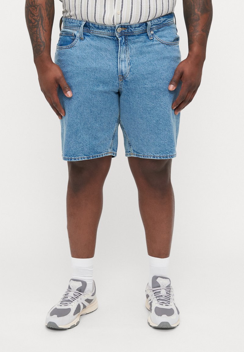 Pantalones cortos de mezclilla en un lavado azul claro con un corte holgado, que cuentan con cinco bolsillos, una cremallera y costuras visibles. Llevados con zapatillas grises y calcetines blancos.