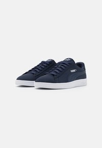 Granatowe trampki z gładką syntetyczną cholewką, białą gumową podeszwą, płaskimi sznurowadłami oraz detalami z logo Puma po bokach i na języku.
