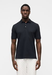 Mustast polosärgist, millel on lühikesed varrukad, kolme nupuga plastron ja sile päriskiht. Kanditud koos mustriliste heledate pükstega.