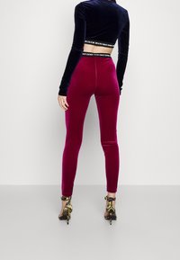 Sammet burgundy leggings med hög midja, figurnära design och slät textur, kombinerat med svarta remsandaler med guld detaljer.