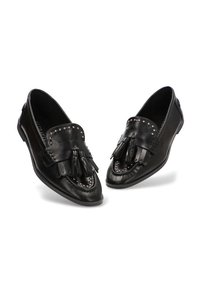 Mocasines de cuero negro con borlas, borde con tachuelas y un brillo suave. Presentan una punta redondeada y suela baja y flexible.