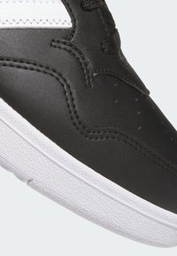 Zapatilla negra de cuero con suela de goma blanca. Presenta detalles de costura y perforaciones en la parte superior. Diseño con cordones para el cierre.
