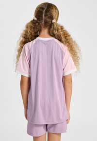 Lichtpaarse sportset bestaande uit een shirt en korte broek met verticale krijtstrepen, een witte kraag en roze raglanmouwen. Het materiaal lijkt ademend en zacht.