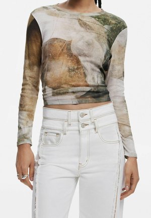 Lyhyt pitkähihainen toppi, jossa on abstrakti maasävyinen kuosi, yhdistetty korkeavyötäröisiin valkoisiin farkkuihin, joissa on kaksipainikkeinen suljenta ja sivukoristelut.