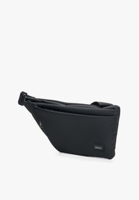 Zwarte schoudertas van zacht, gewatteerd materiaal. Heeft een slanke, geometrische vorm met een ritssluiting en een reliëflogo aan de ene kant.
