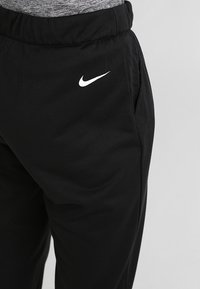 Zwarte sportbroek van zacht materiaal, met een wit Nike-logo aan de zijkant en een elastische tailleband met zakken.