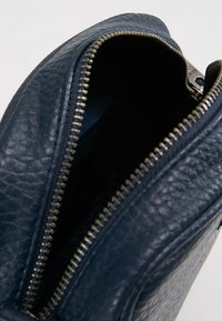 Interiér kabelky z tmavě modré kůže se zavíráním na zip. Texturovaný materiál a kontrastní kovový zip. Uvnitř hladká tmavá podšívka.