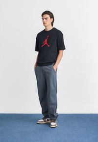 Must must t-särk musta Jumpman logo punasega, kokku sobitatud lõtvade hallide pükstega ja halli-valgete tossudega kollaste paeltega.