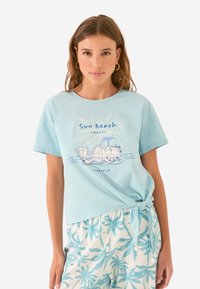 T-shirt en coton bleu clair à manches courtes. Présente un graphisme de personnage détendu avec le texte "Sun Beach Amalfi" en dessous.
