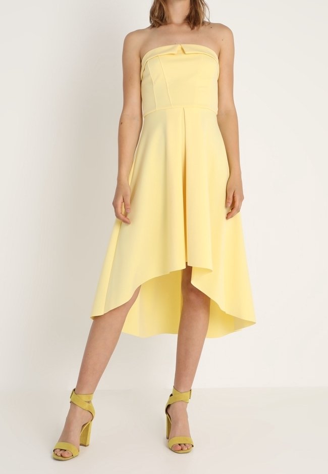 Un vestido amarillo sin tirantes con un dobladillo asimétrico y un detalle de lazo en la parte delantera, combinado con sandalias de tacón alto amarillas a juego.