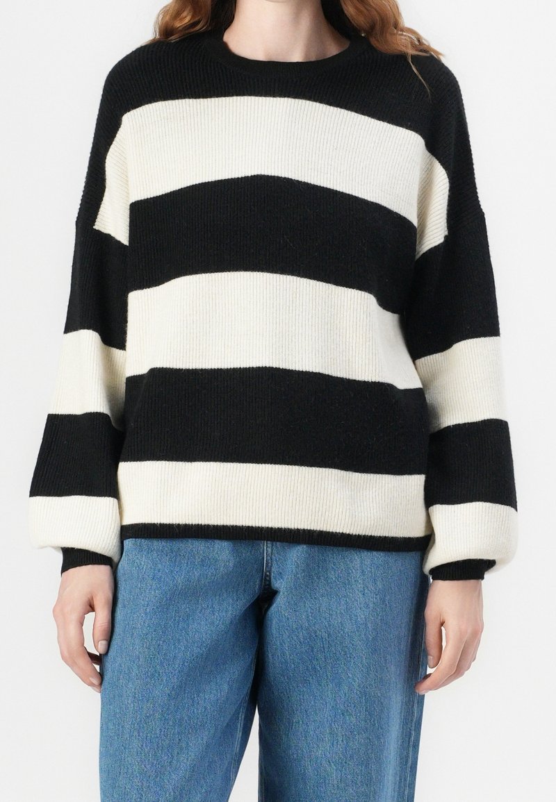 Schwarz-cream gestreifter Pullover mit gerippter Textur, Rundhalsausschnitt und übergroßen Ärmeln, kombiniert mit blauen Jeans.