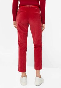 Rote Cordhosen mit schmaler Passform und seitlichen Taschen, mit glatter Textur, Gürtelschlaufen und gespaltenem Saum, kombiniert mit weißen Sneakern.