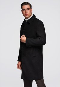 Schwarzer Wollmantel mit einem strukturierten Kragen, Frontknöpfen und Seitentaschen, mit glatter Textur und taillierter Passform.