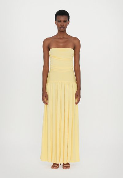 Geel strapless jurkje met een verzameld lijfje, vloeiende geplooide rok, gemaakt van lichtgewicht stof; gestyled met eenvoudige sandalen.