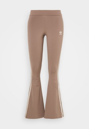 Leggings bruns évasés en tissu extensible, avec des bandes latérales blanches et un petit logo blanc sur la cuisse gauche. Texture lisse.