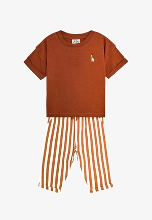Chemise à manches courtes couleur rouille avec petit logo girafe, associée à un pantalon à rayures verticales blanches et rouille avec revers aux chevilles.