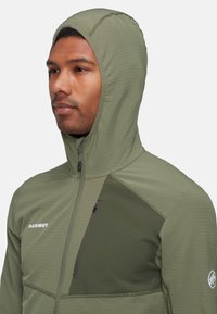 Huvjacka i olivgrön, tillverkad av lätt material. Har en dragkedjeförsedd bröstficka, kontrasterande paneldesign och logotypdetalj.