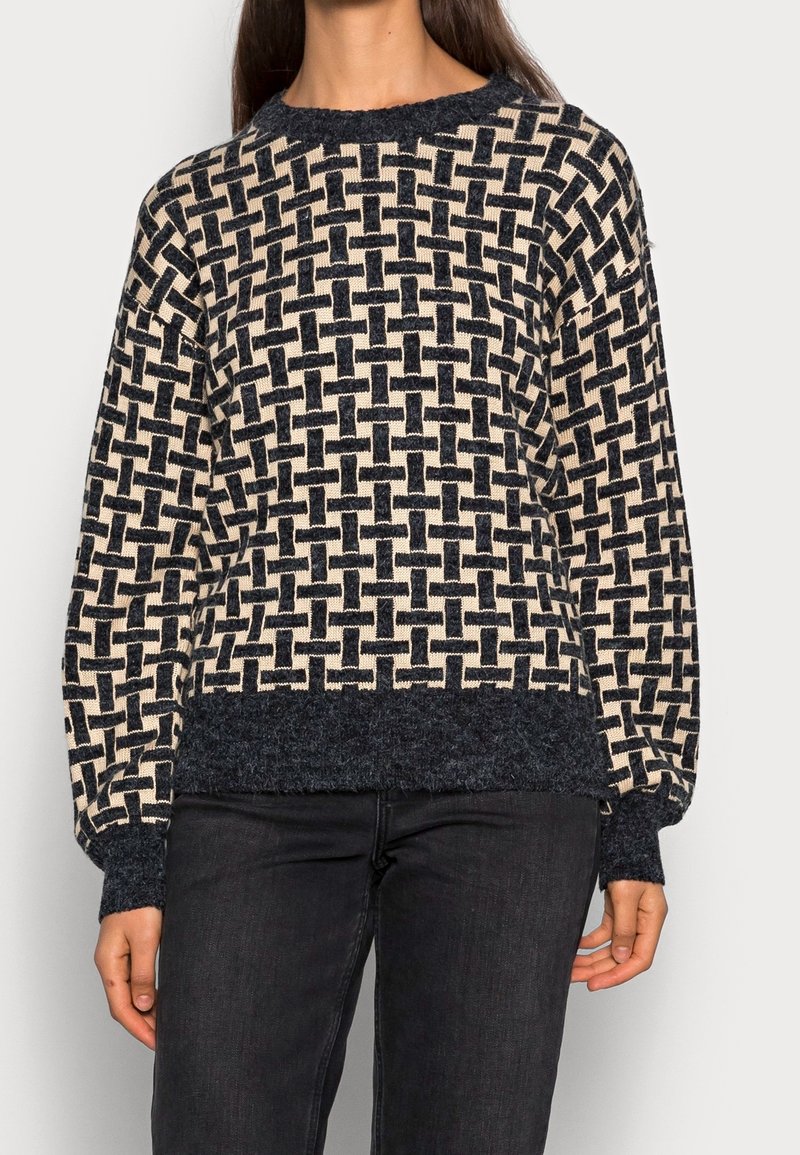 Pull en tricot avec un motif entrelacé crème et bleu foncé, col rond, ourlet texturé et manches longues. Fabriqué en tissu doux.