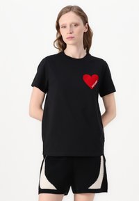 T-shirt noir à manches courtes avec un graphique de cœur rouge et le mot "FUTURE" sur la poitrine gauche. Fabriqué en coton doux avec une coupe décontractée.
