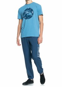 Light blue cotton t-shirt with a circular graphic design; navy blue sweatpants with a white logo print on the side; black sneakers.