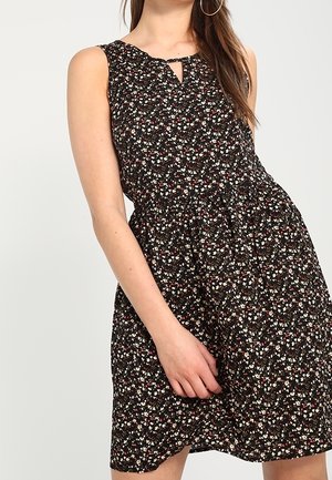 Robe noire sans manches avec un motif floral en blanc, rouge et vert. Elle présente une ouverture en goutte d'eau à l'avant et une taille froncée pour une silhouette évasée.
