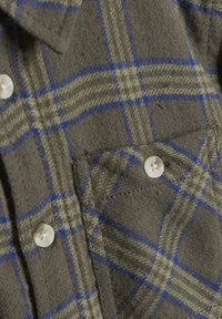 Flanellen overhemd in olijfgroen met een blauw en geel ruitpatroon. Bevat witte knopen en een borstzak met zichtbare stikseldetails.
