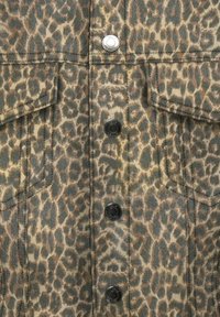 Chemise à imprimé léopard en teintes beige et marron avec des boutons noirs, comportant deux poches poitrine et des détails cousus. Tissu texturé.