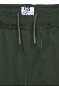 Ciemnozielone spodnie na gumie z troczkami i widoczną białą etykietą z napisem "Weekend Offender" oraz logo korony.
