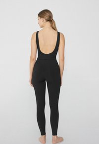 Czarny bodysuit bez rękawów z niskim plecami, dopasowany krój, gładka faktura i długie nogawki. Minimalistyczny i w jednolitym kolorze.