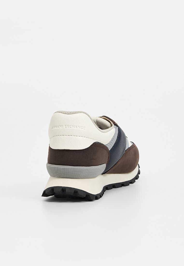 Zapatillas deportivas marrones y azul marino que presentan una mezcla de materiales lisos y texturizados, con una suela de goma y un talón acolchado para mayor comodidad.