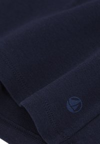 Marineblauwe stof met een gladde textuur, voorzien van een klein rond logo in een iets donkerdere schaduw van blauw en net afgewerkte naden langs de randen.