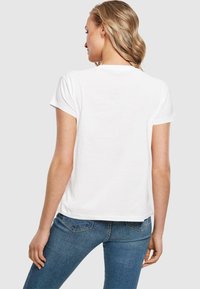 Weißes Baumwoll-T-Shirt mit kurzen Ärmeln, einem Rundhalsausschnitt und einer lockeren Passform, kombiniert mit blauen Jeans. Ein schlichtes, einfarbiges Design.