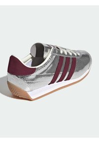 Hõbedased nahast tossud läikiva lõpetusega, punaste triipudega, valgete paeltega ja kummist kummipohjaga. Omab pehmendatud krae mugavuse tagamiseks.